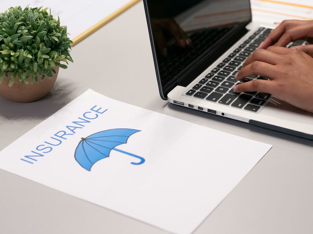 Person works on a laptop with insurance document on the desk next to them.