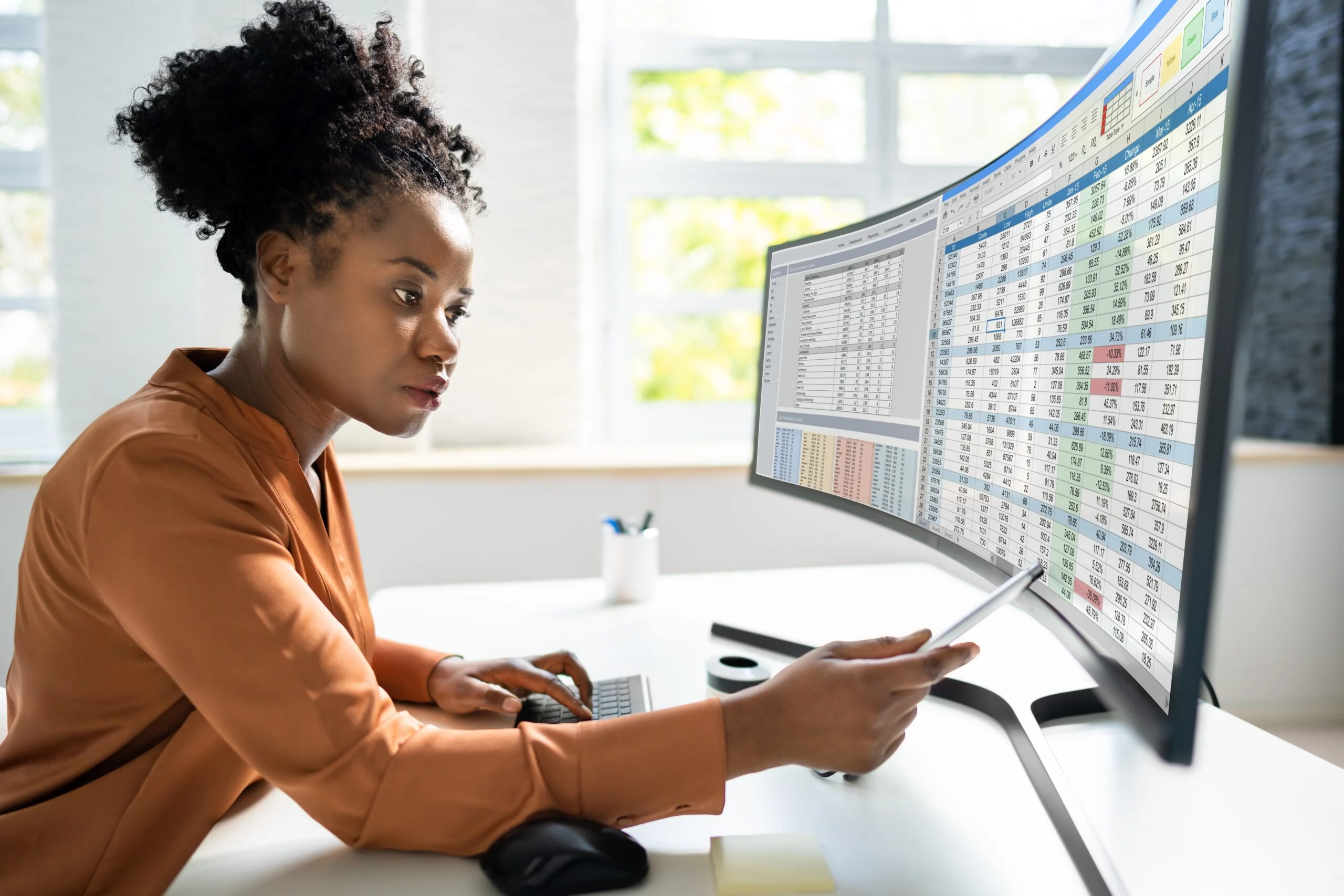 A data analyst reviews spreadsheet data on a large curved monitor, representing the challenge of managing and governing data at scale.