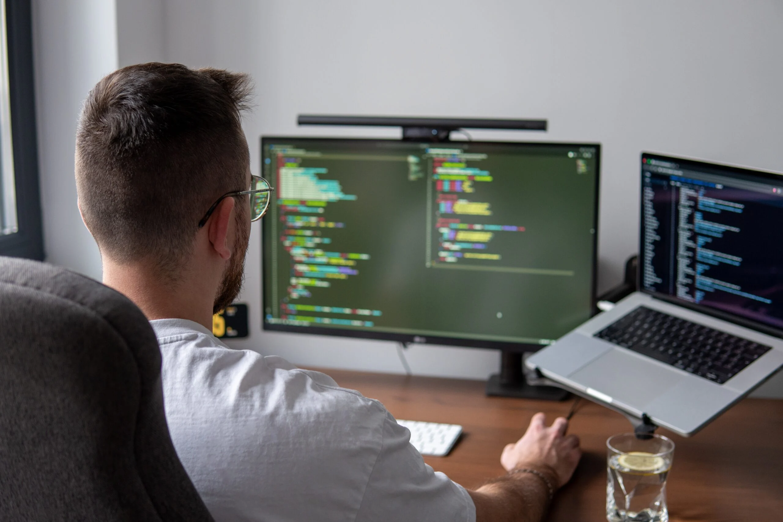 Developer reviewing code on dual monitors while using an AI agent to scan a MongoDB collection for PII and query performance issues